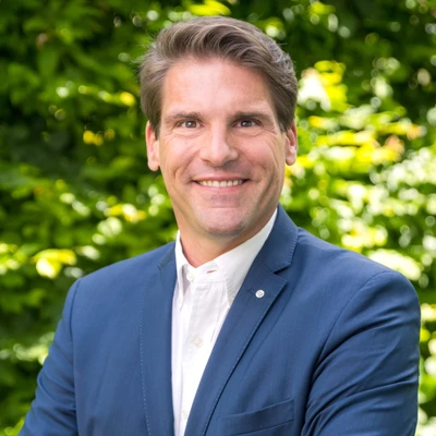 Mann im Anzug lächelt vor grünem Hintergrund.