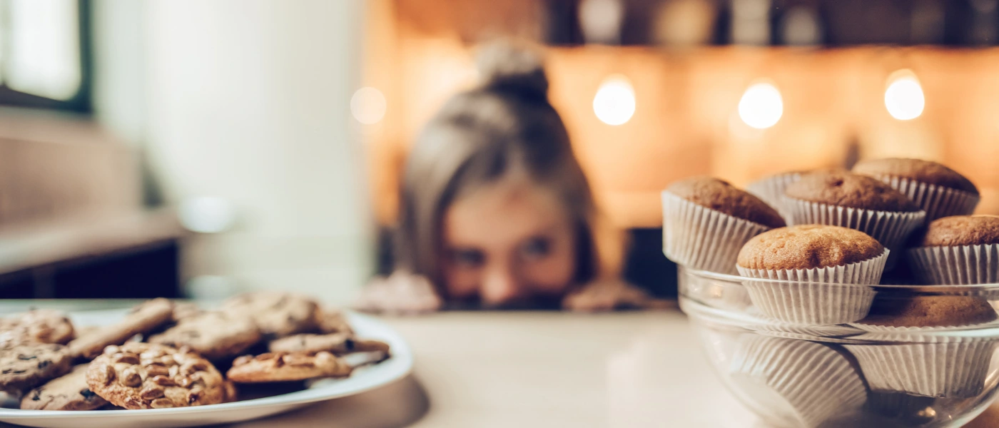 Kind schaut sehnsüchtig auf Kekse und Muffins