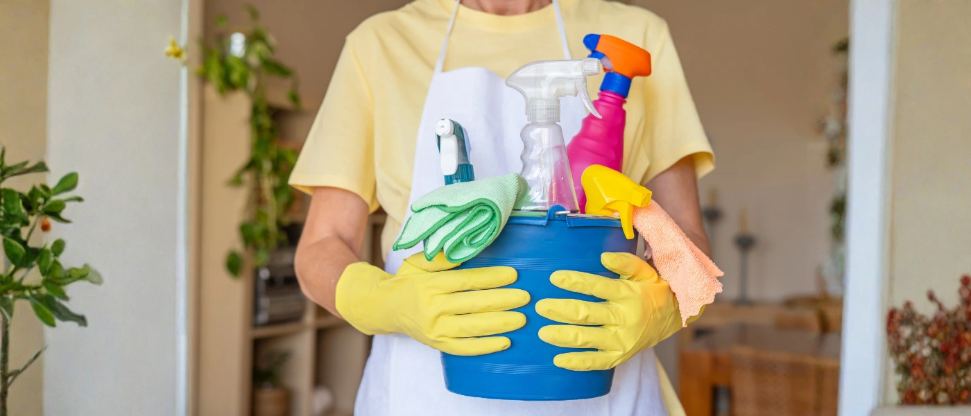 Person mit Reinigungseimer und Putzmitteln.