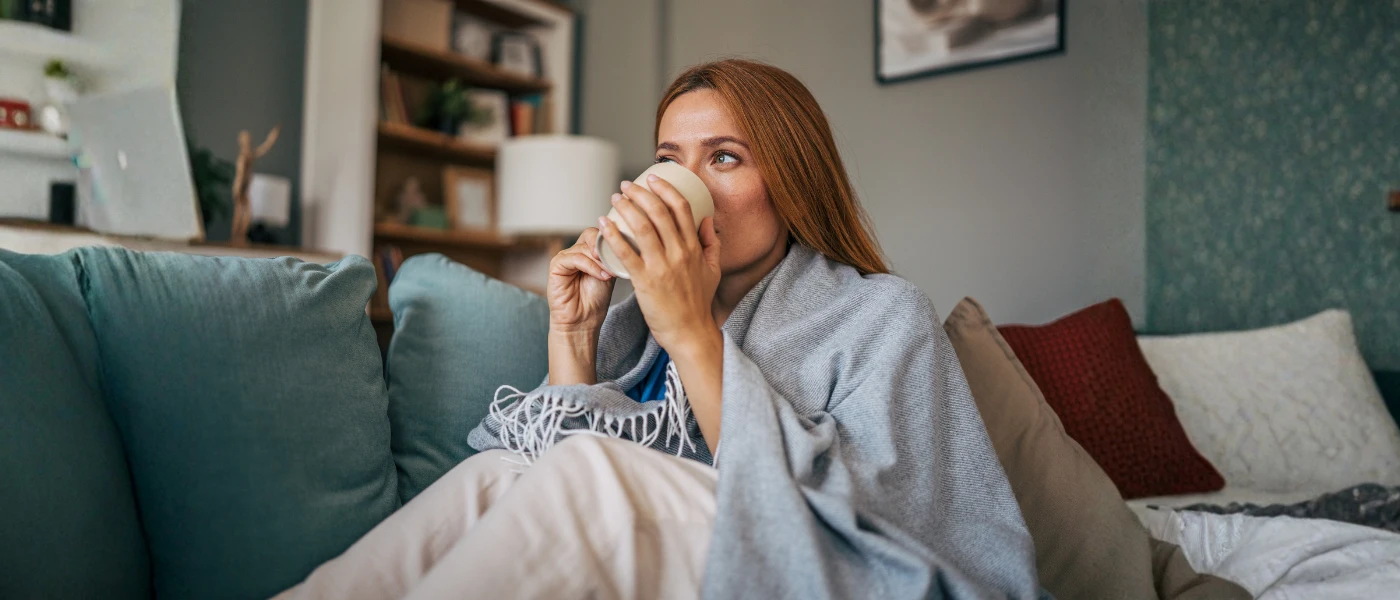 Frau trinkt Tee auf dem Sofa sitzend.